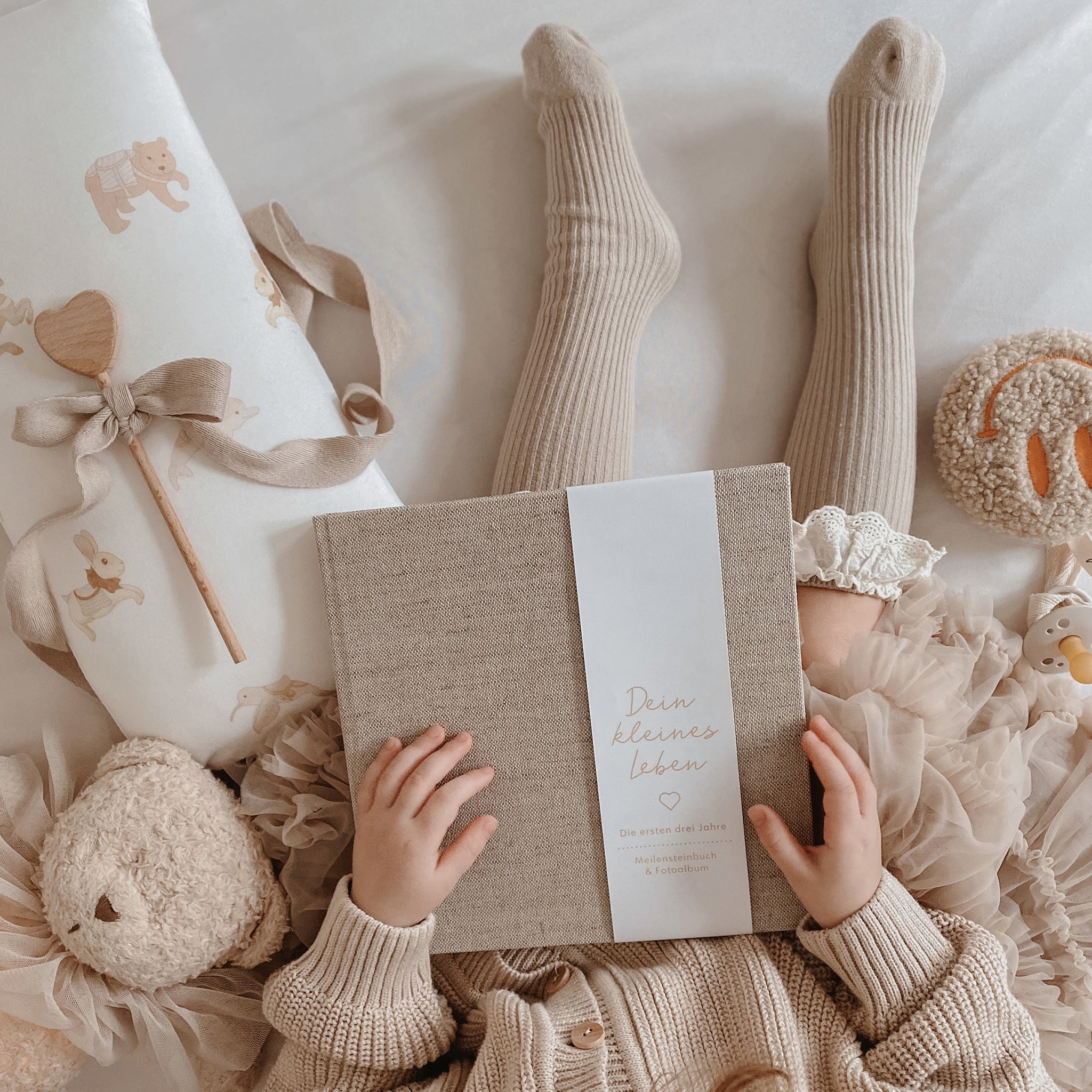 Arragement: Babybuch aus Leinenstoff mit den Händen eines Mädchens